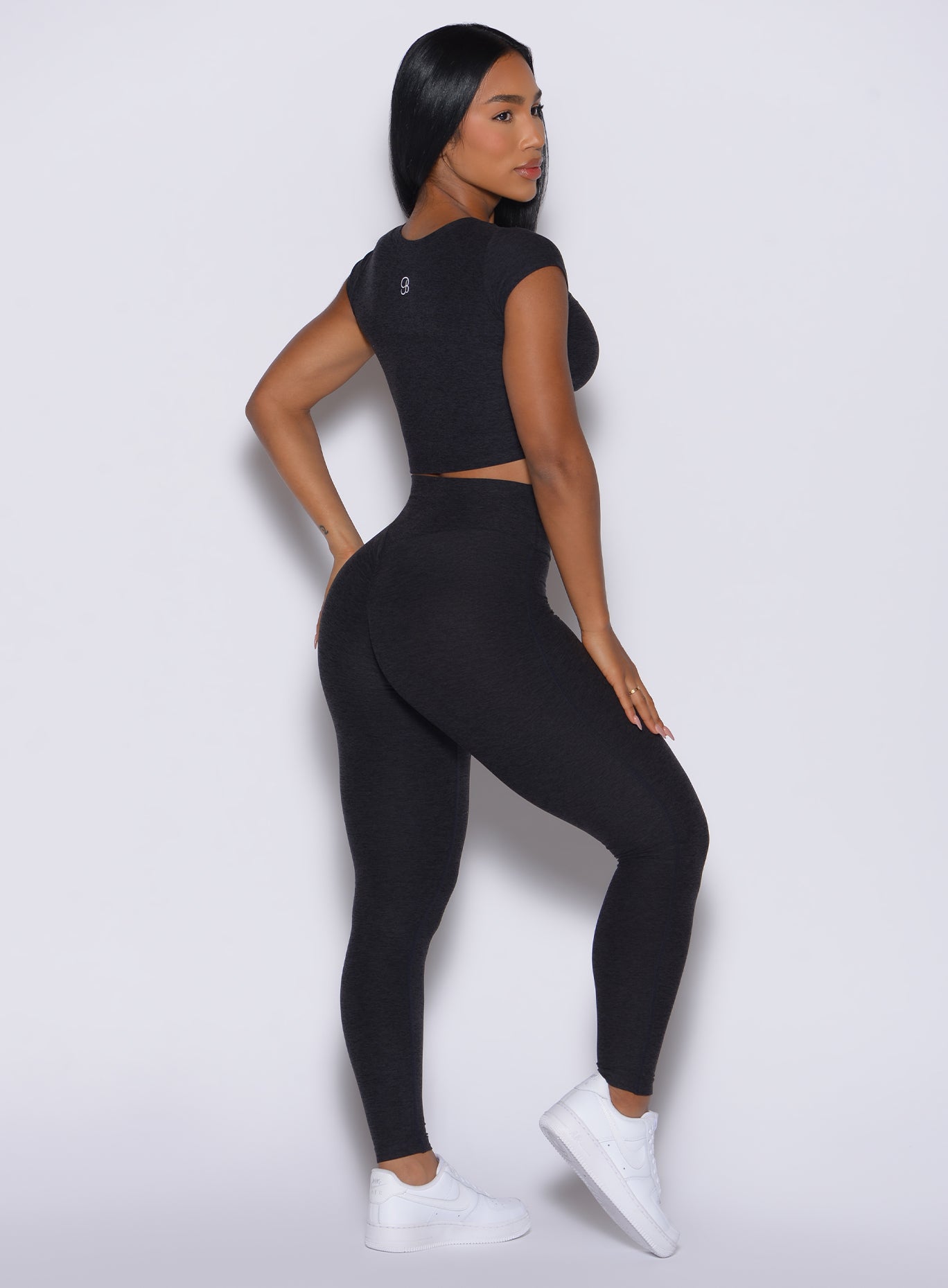 back profile of model facing to her right wearing the Movement Leggings in Onyx color and a matching Tee