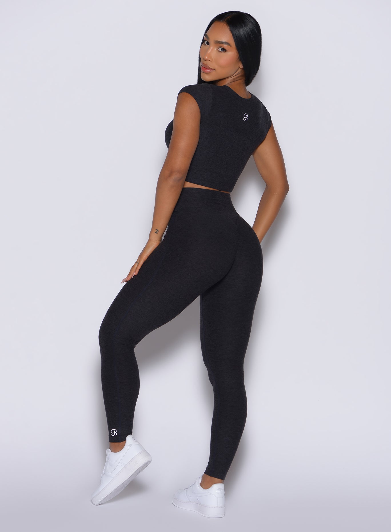 back profile of model angled left wearing the Movement Leggings in Onyx color and a matching Tee