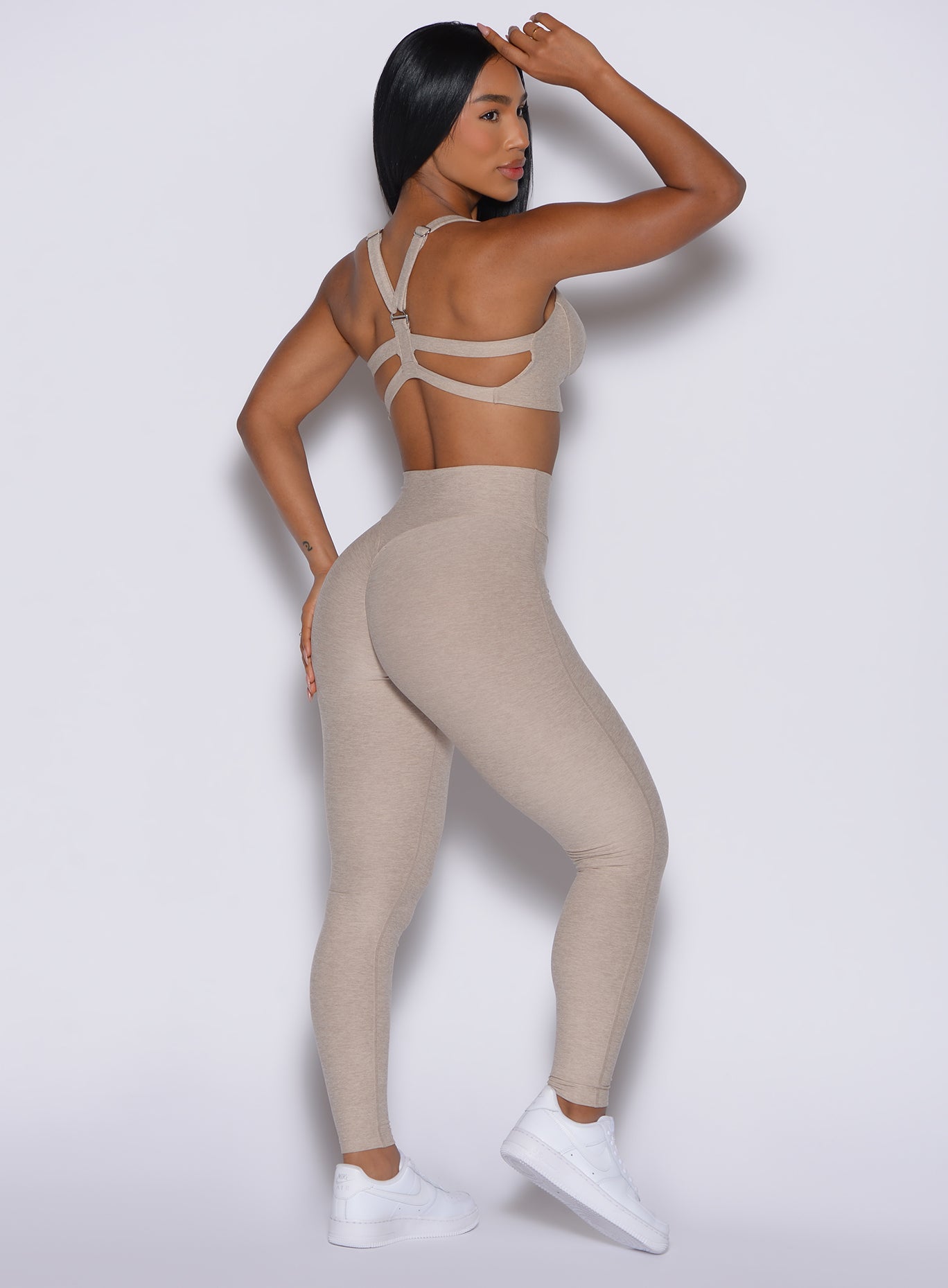 back profile of model angled to her right wearing the Movement Leggings in Taupe color and a matching Sports Bra