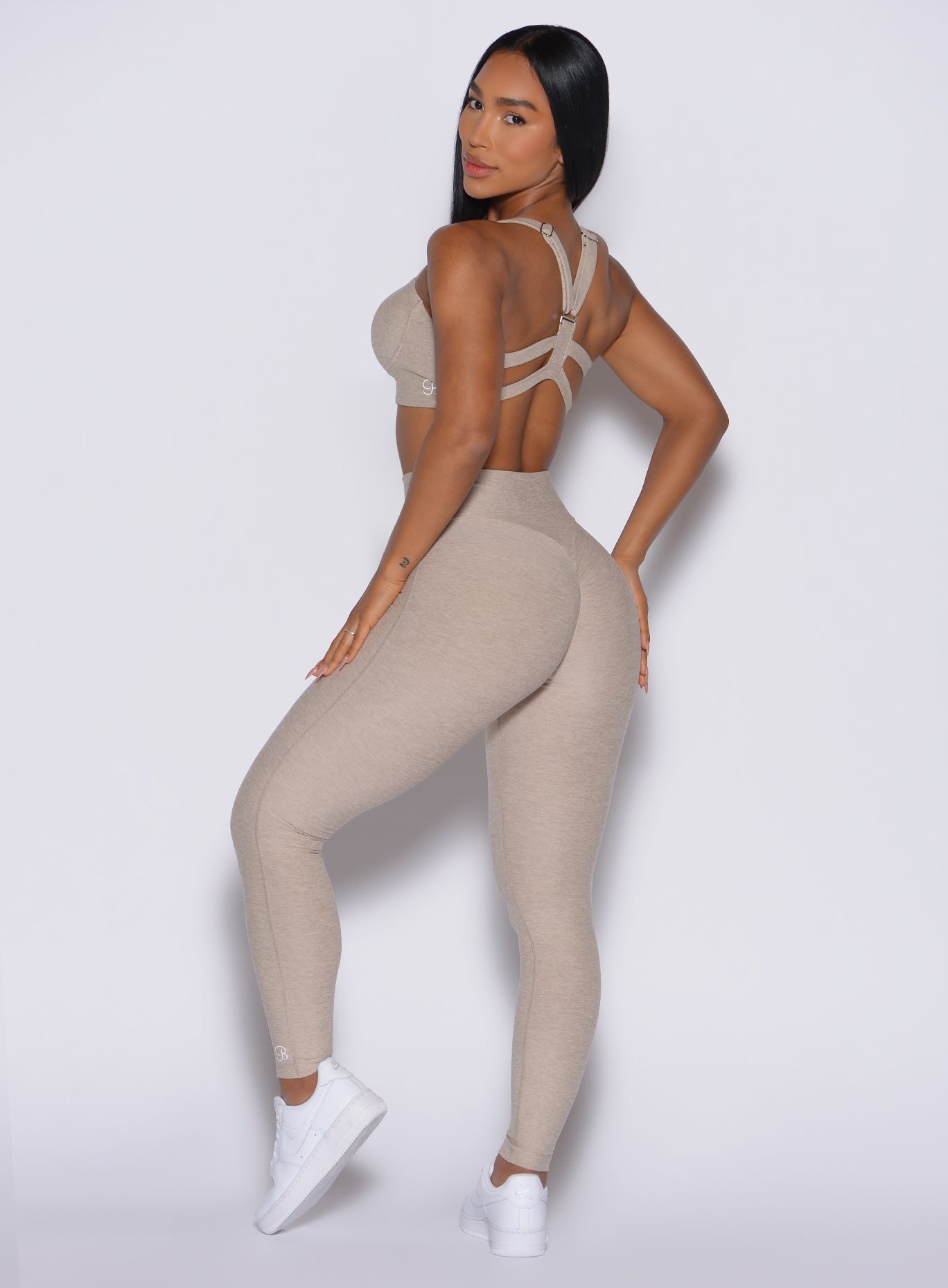 back profile of model angled to her left wearing the Movement Leggings in Taupe color and a matching Sports Bra