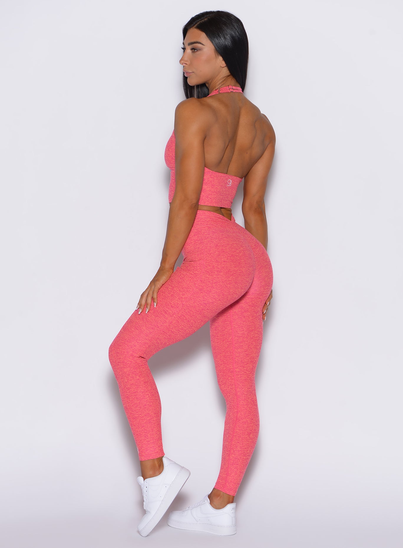 Left side profile view of a model wearing our V back leggings in Neon Tangerine Shock color along with a matching bra