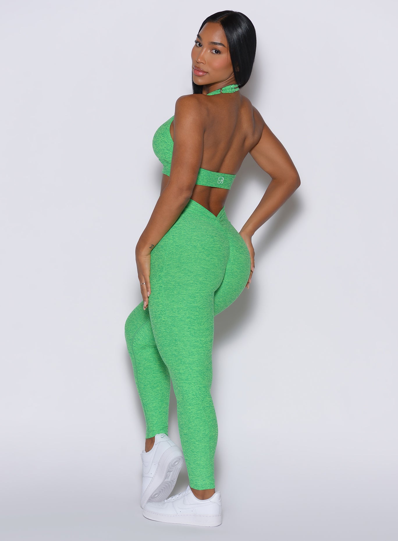 left side profile view of a model facing to her left wearing our V back leggings in Neon Miami Beach color along with a matching bra