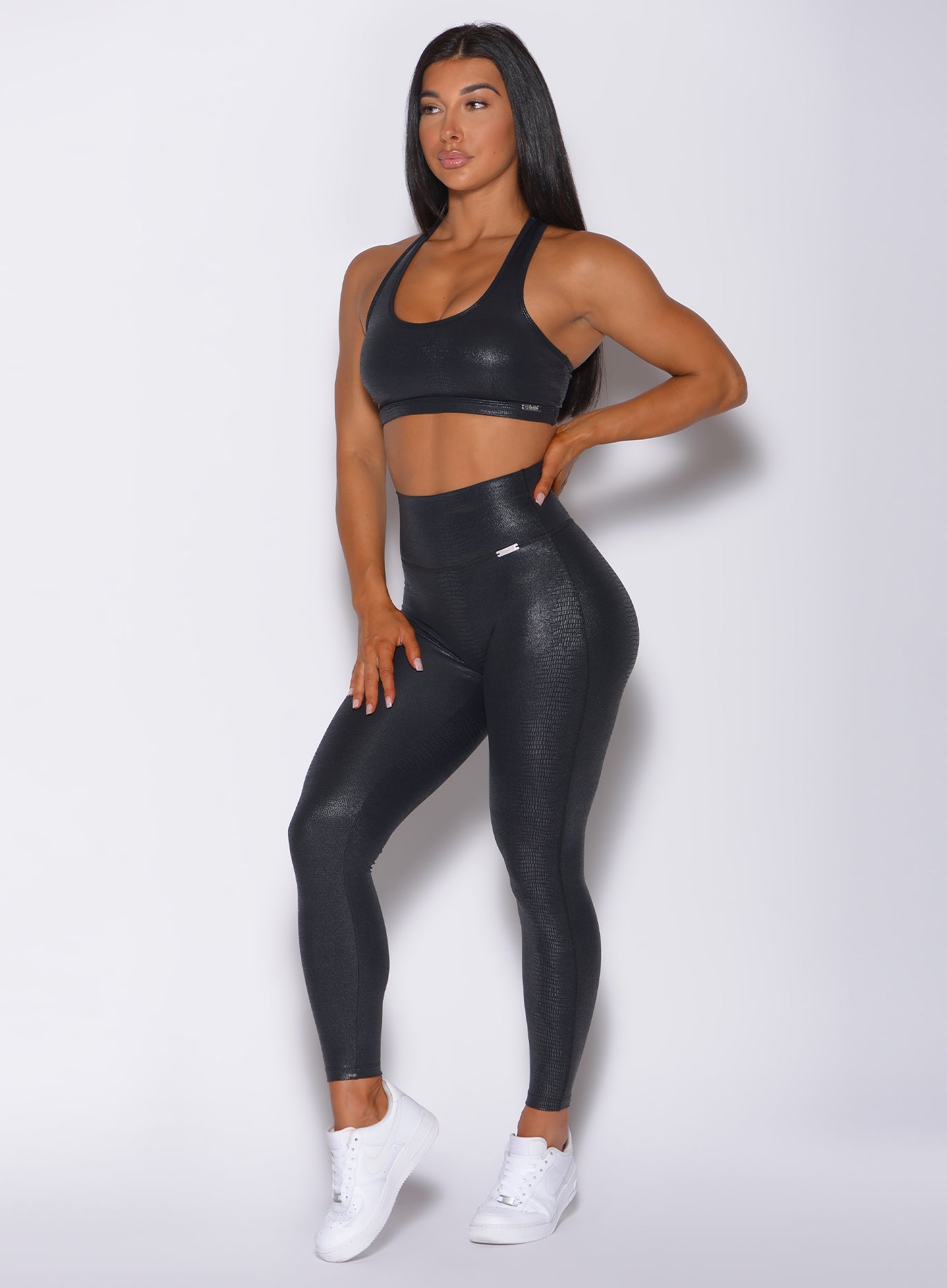 Left side profile view of a model angled left wearing our shine leggings in black python color and a matching sports bra