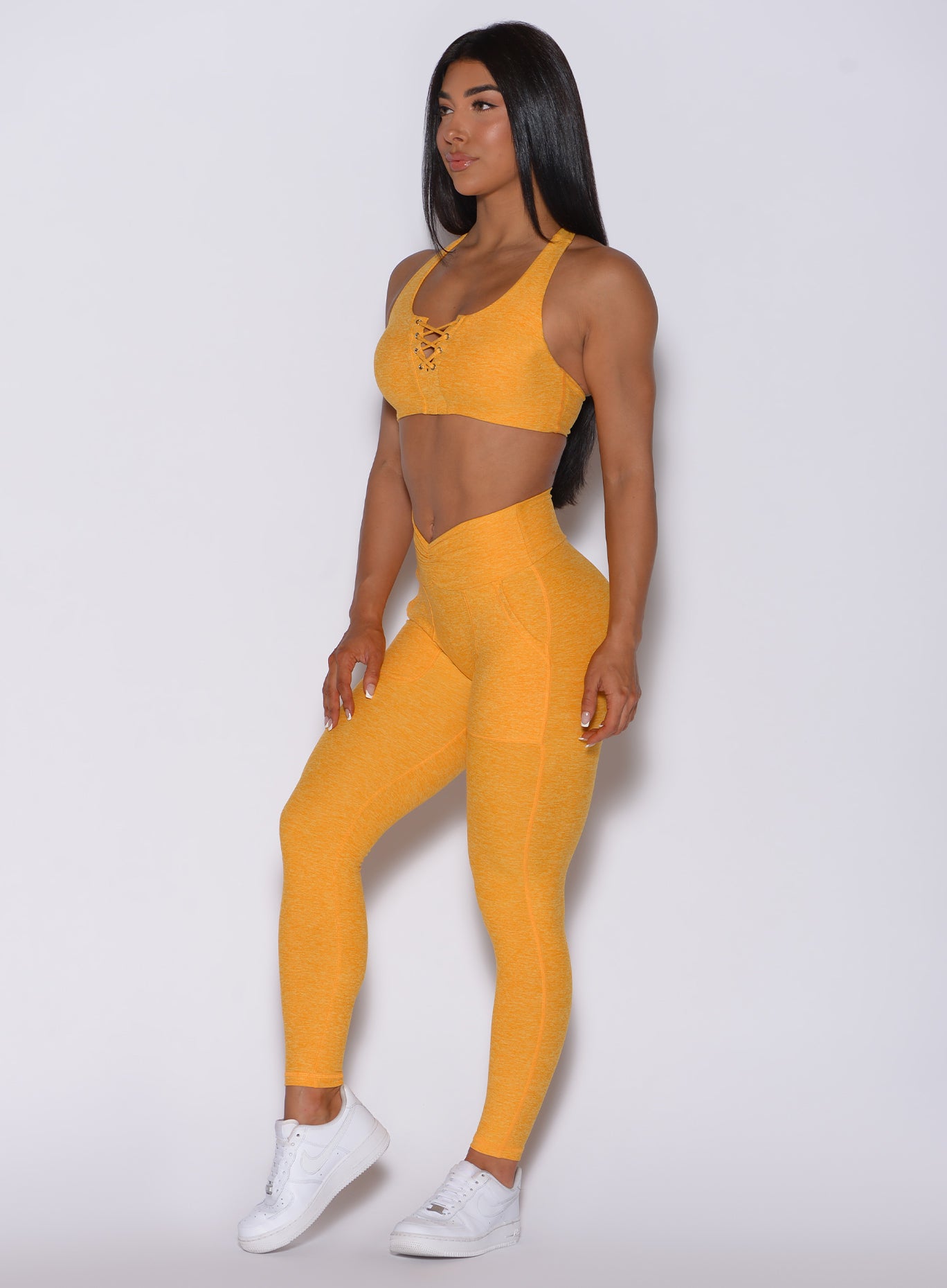 Left side profile view of a model angled slightly to her left wearing our V scrunch leggings in sinkissed color and a matching bra