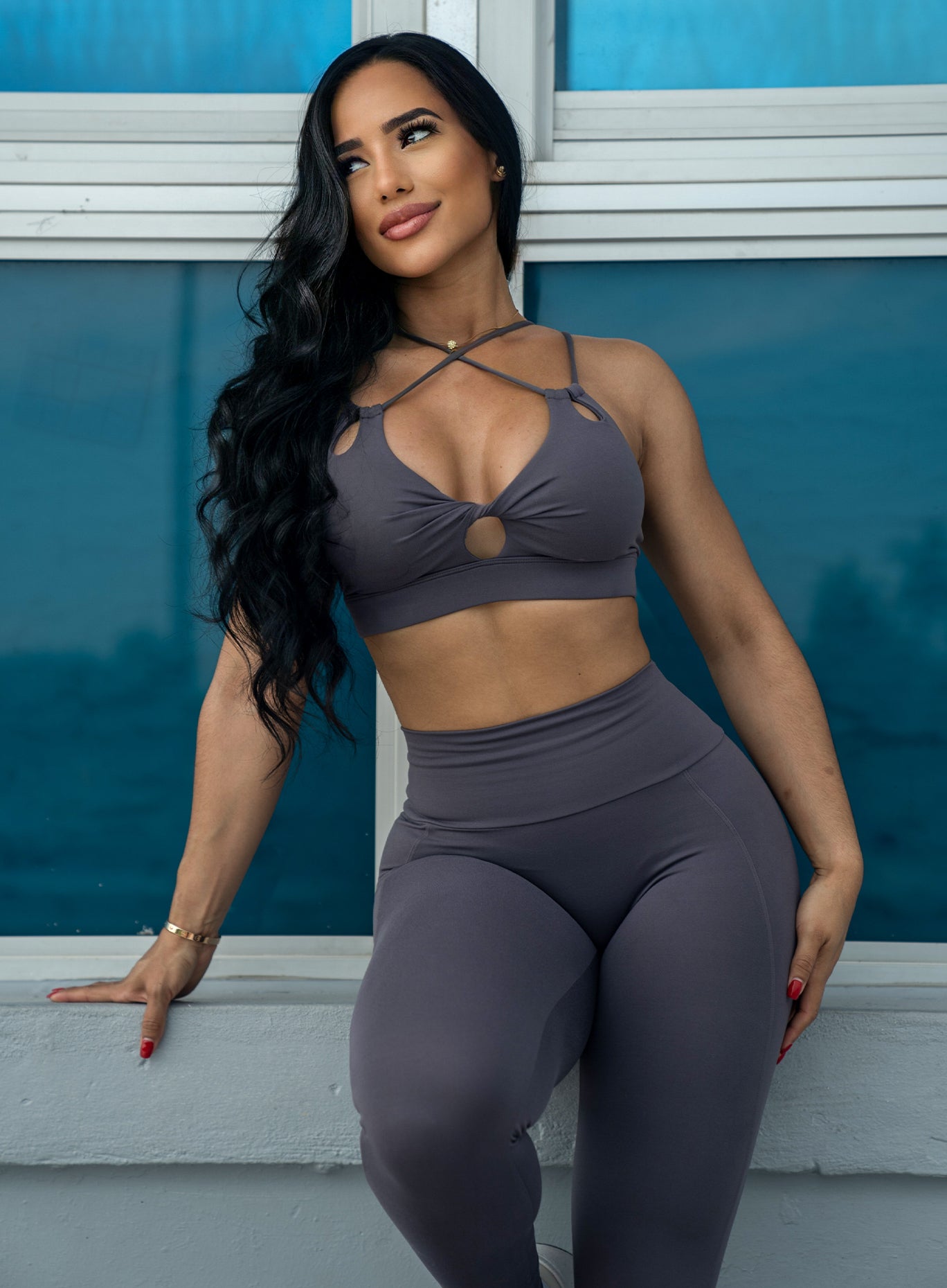 Front profile of a model leaning on a wall wearing our twist sports bra in gray smoke color and a matching leggings