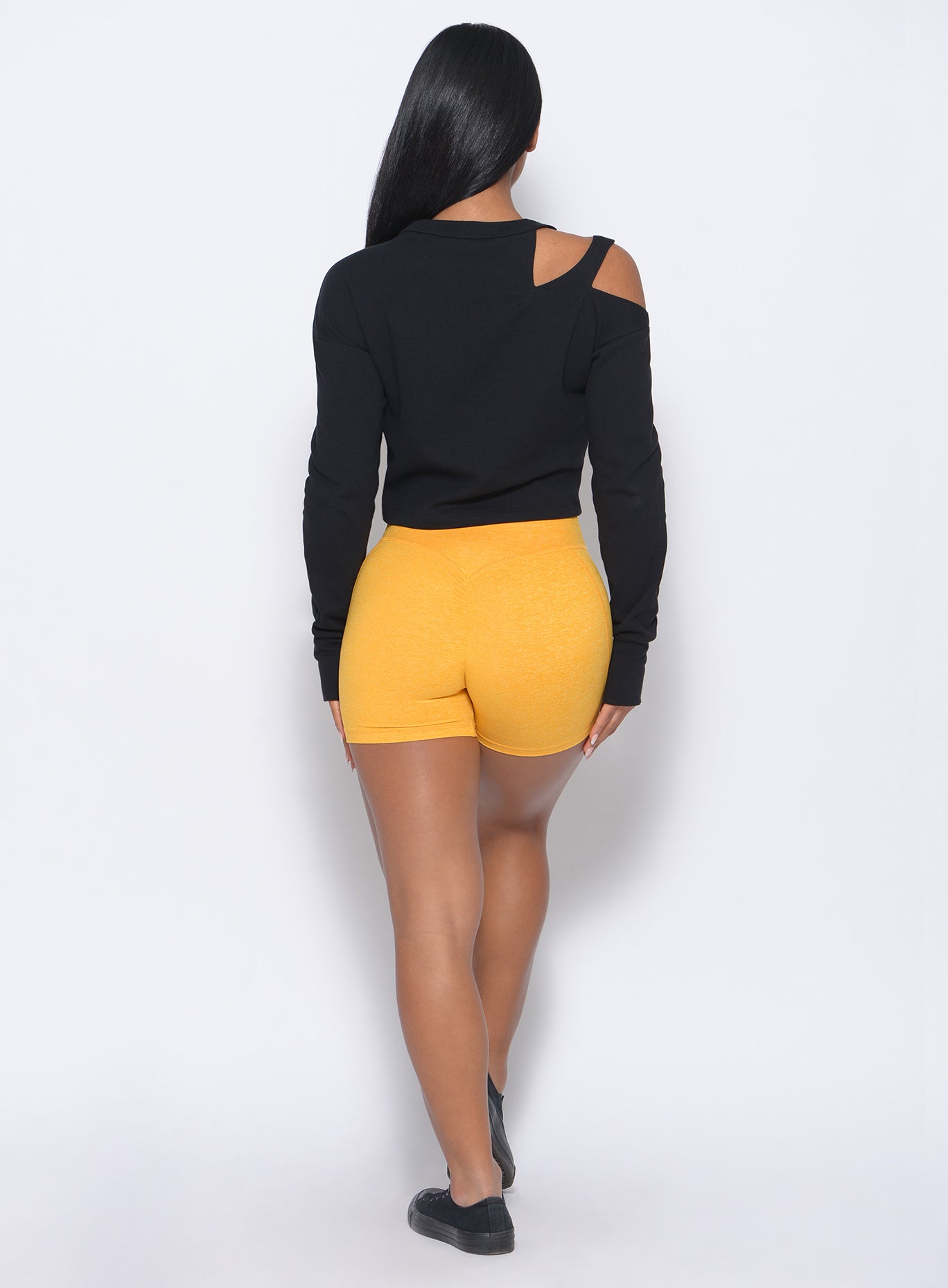 Back profile view of the model in our tiny waist shorts in sunkissed color and a black pullover