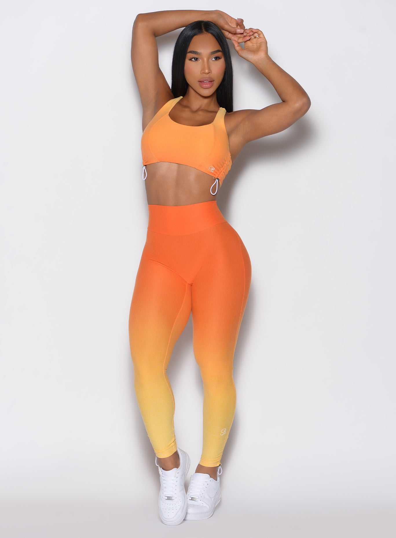 front profile view of a model facing forward with her hands over her head wearing our toggle leggings in Ombre Hawaiian Punch color along with the matching sports bra