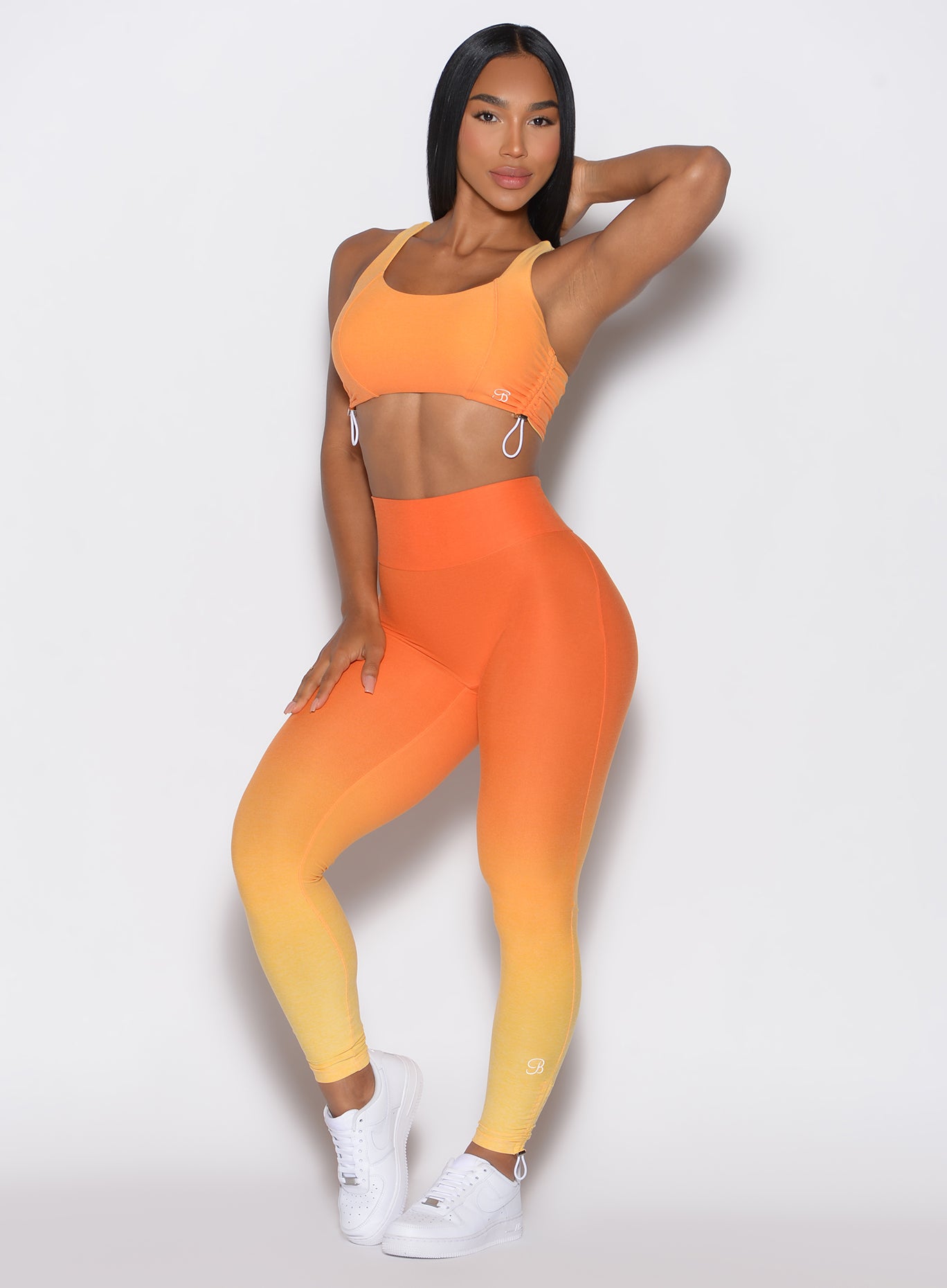 front profile view of a model with her left hand over her neck wearing our toggle leggings in Ombre Hawaiian Punch color along with the matching sports bra