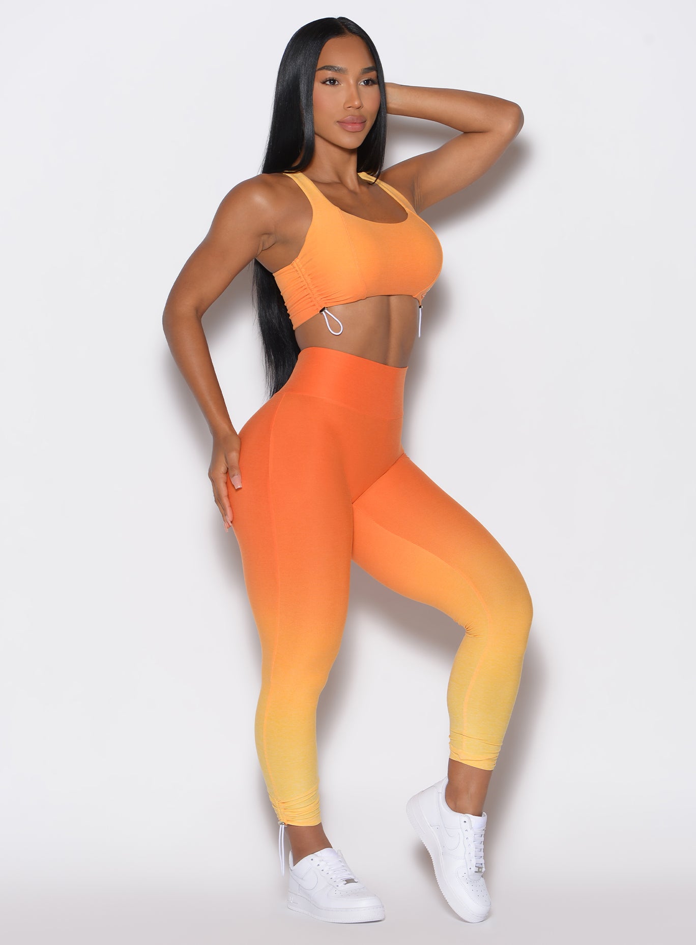 right side profile view of a model angled slightly to her right wearing our toggle leggings in Ombre Hawaiian Punch color along with the matching sports bra