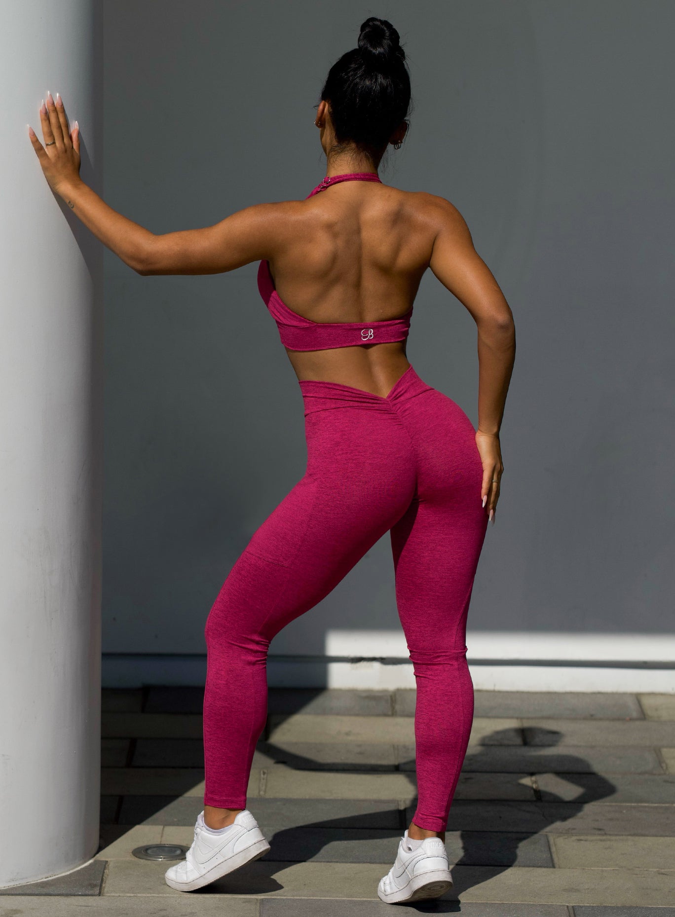 back profile view of a model outside wearing our V back leggings in fuchsia color along with the matching bra